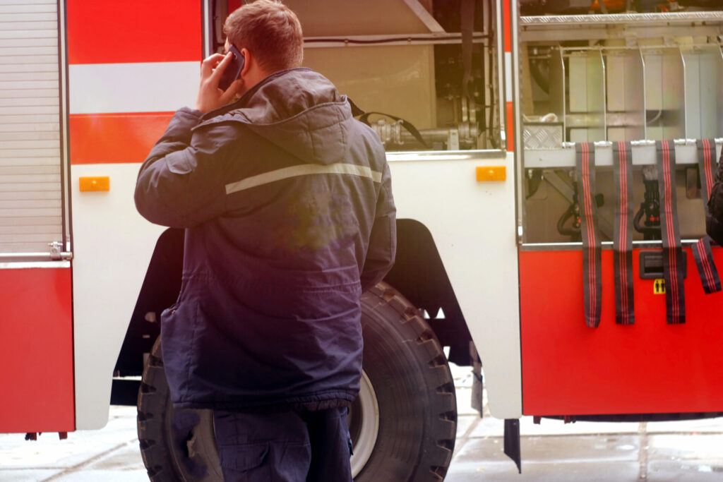 A man standing next to a firetruck, talking into a cellphone at a wildfire site