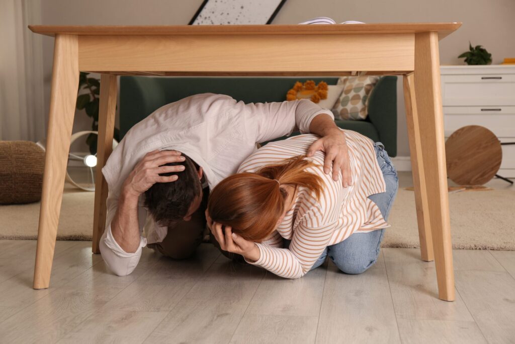 A couple experiencing an earthquake takes cover under a table.