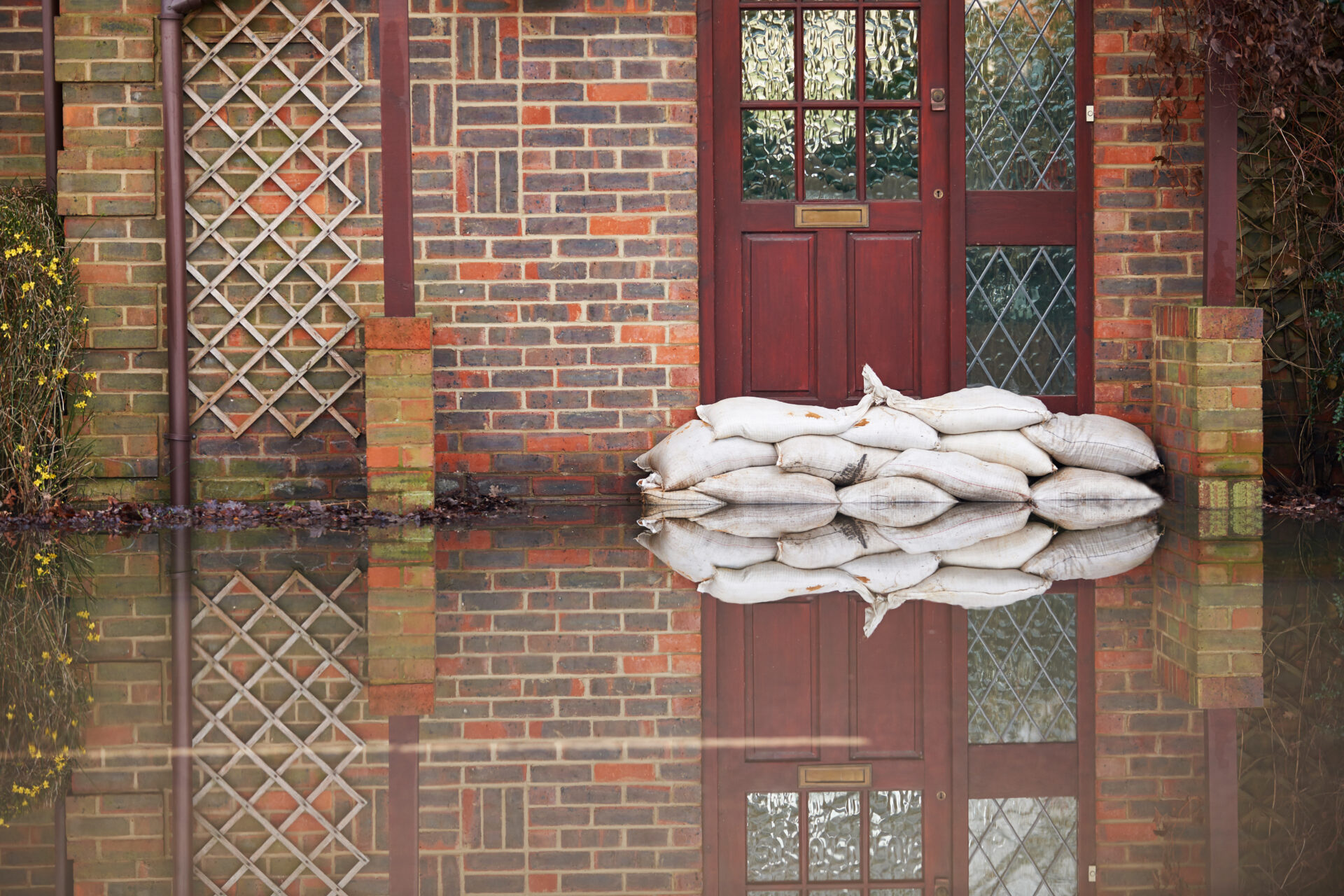 Sandbags are piled outside the front door of a home with a flooded front porch.