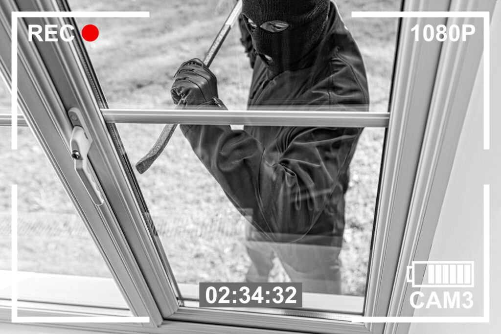 A closed-circuit television image of a potential thief using a crowbar to open a locked window