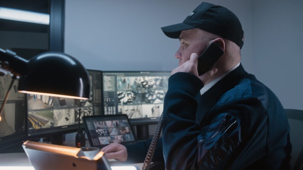 A security officer with CCTV screens on the phone with law enforcement